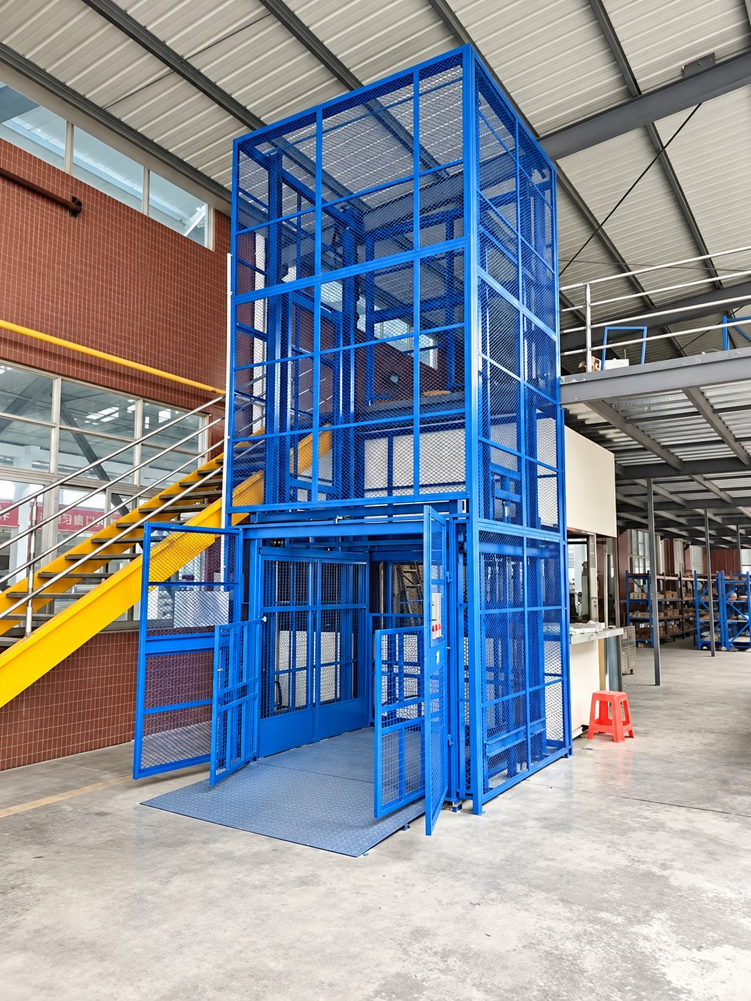 Blue hydraulic goods lift with mesh enclosure in a factory workshop