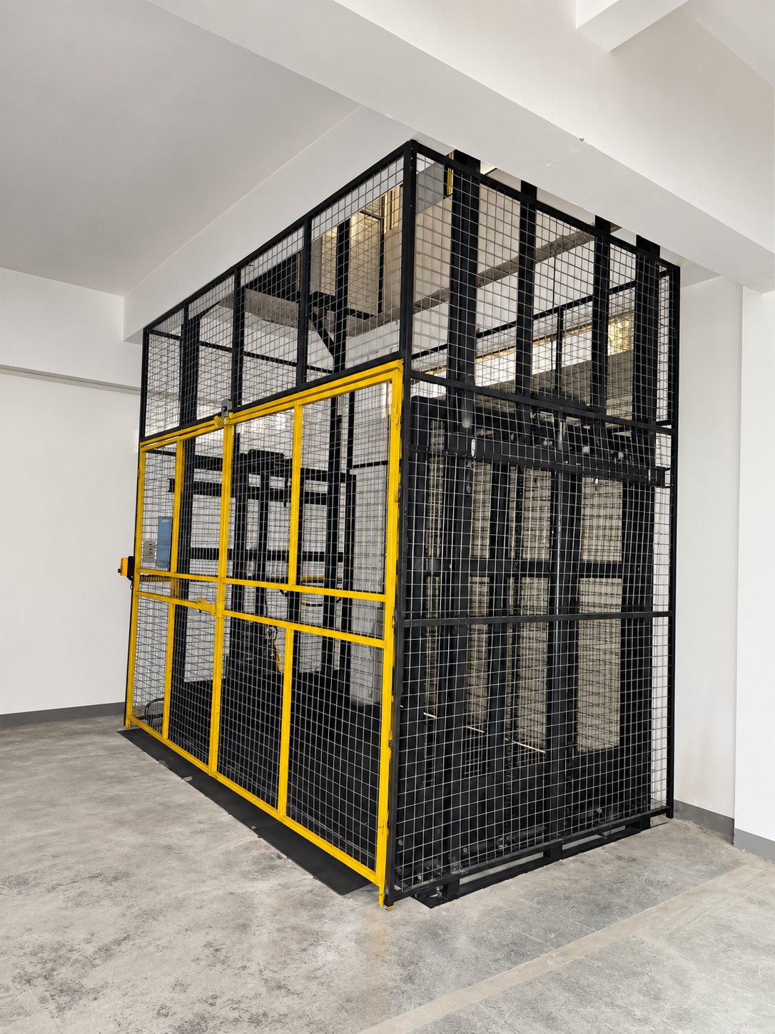 Enclosed industrial freight lift with black mesh panels and yellow landing gate