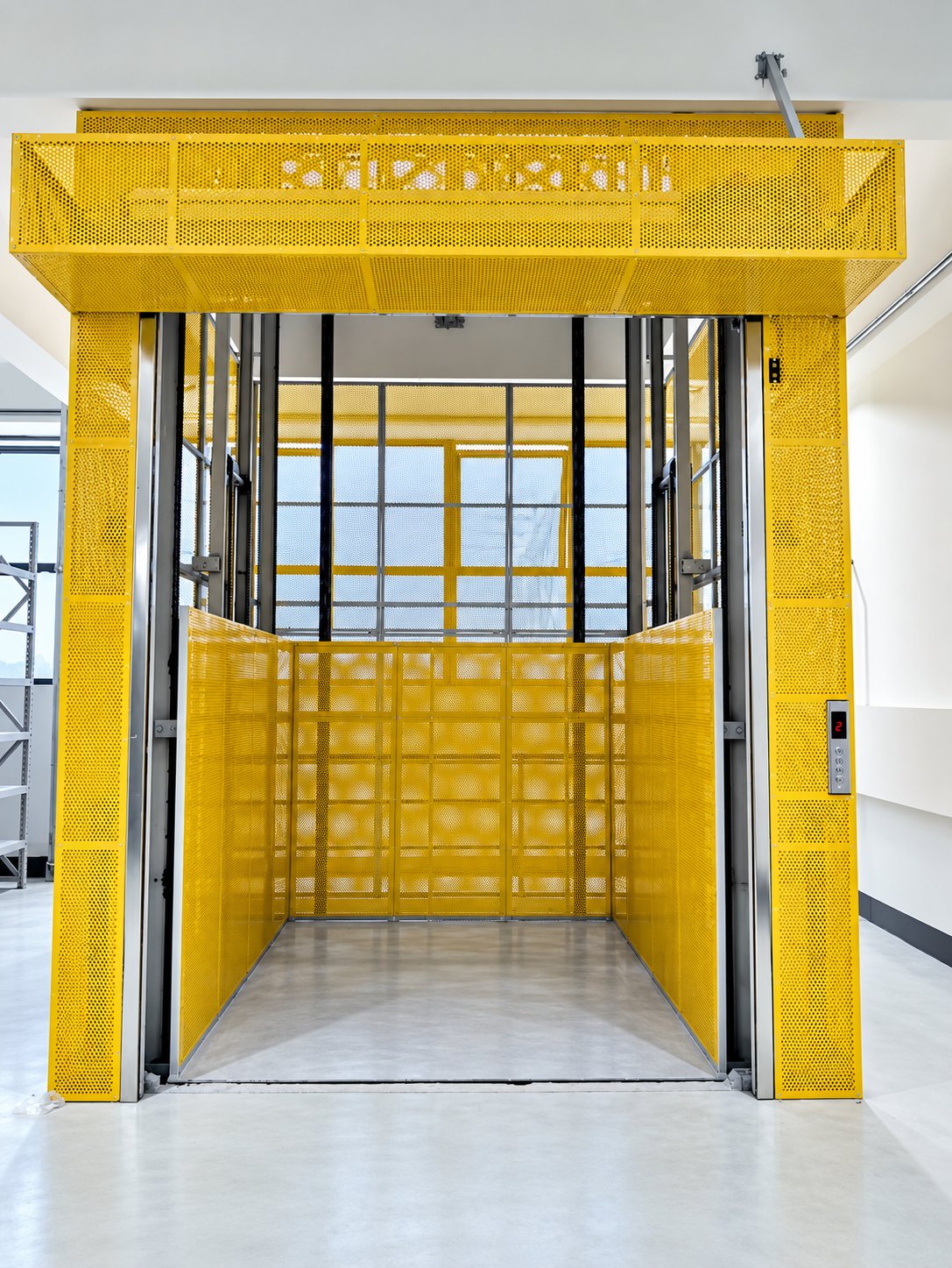 Industrial hydraulic cargo lift with yellow perforated safety enclosure