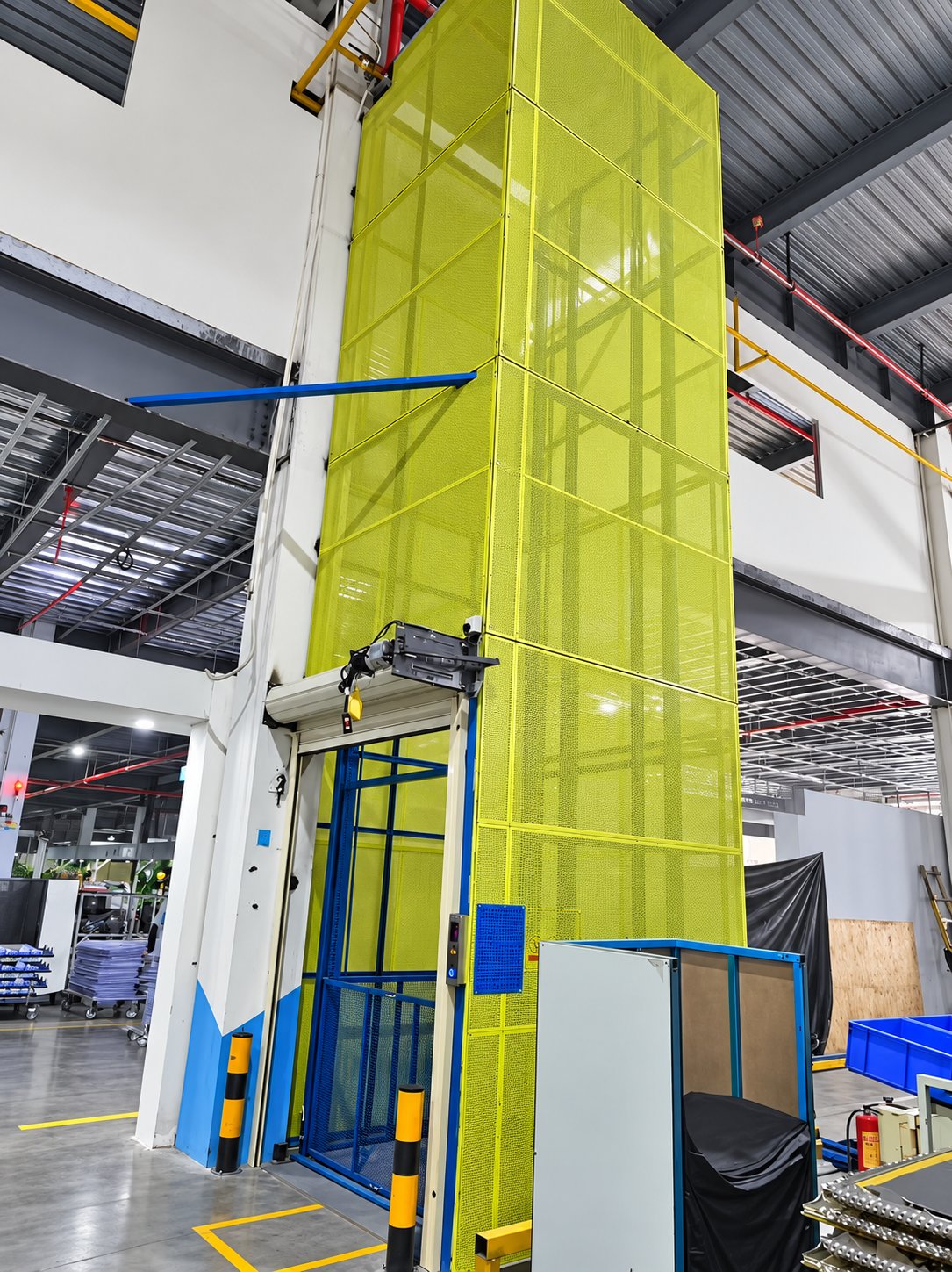 Warehouse vertical cargo lift installed inside a tall perforated steel safety shaft